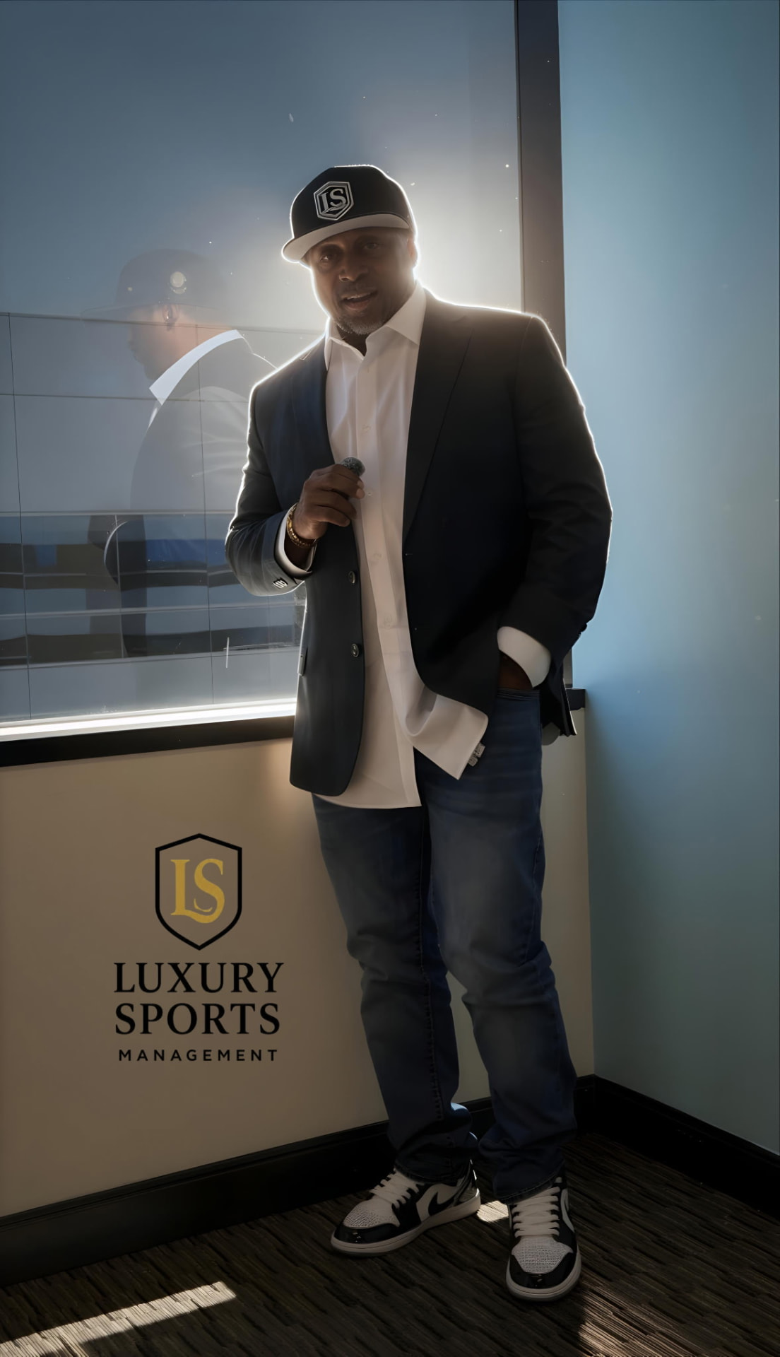 Lamont Hewitt standing beside the Luxury Sports Management crest